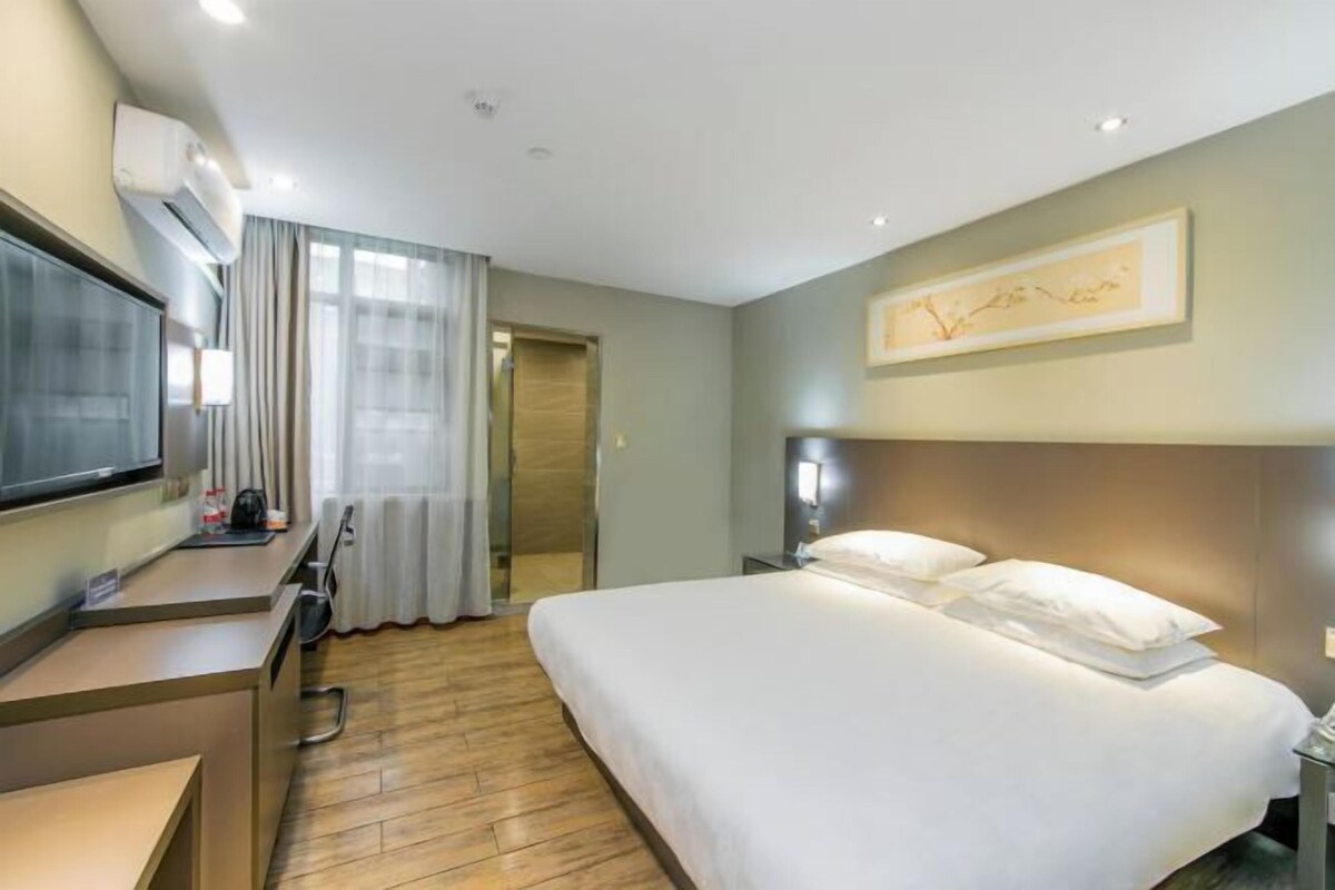 A hotel room with a bed, a desk, a television, and a window with curtains.