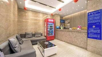 A hotel lobby with a reception desk, a seating area with a sofa, a coffee table, and a vending machine.