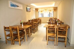 A dining area with multiple wooden tables and chairs, a television mounted on the wall, and a window with curtains. - Superior Hotel (Ziyuan Bus Station) (Ziyuan)