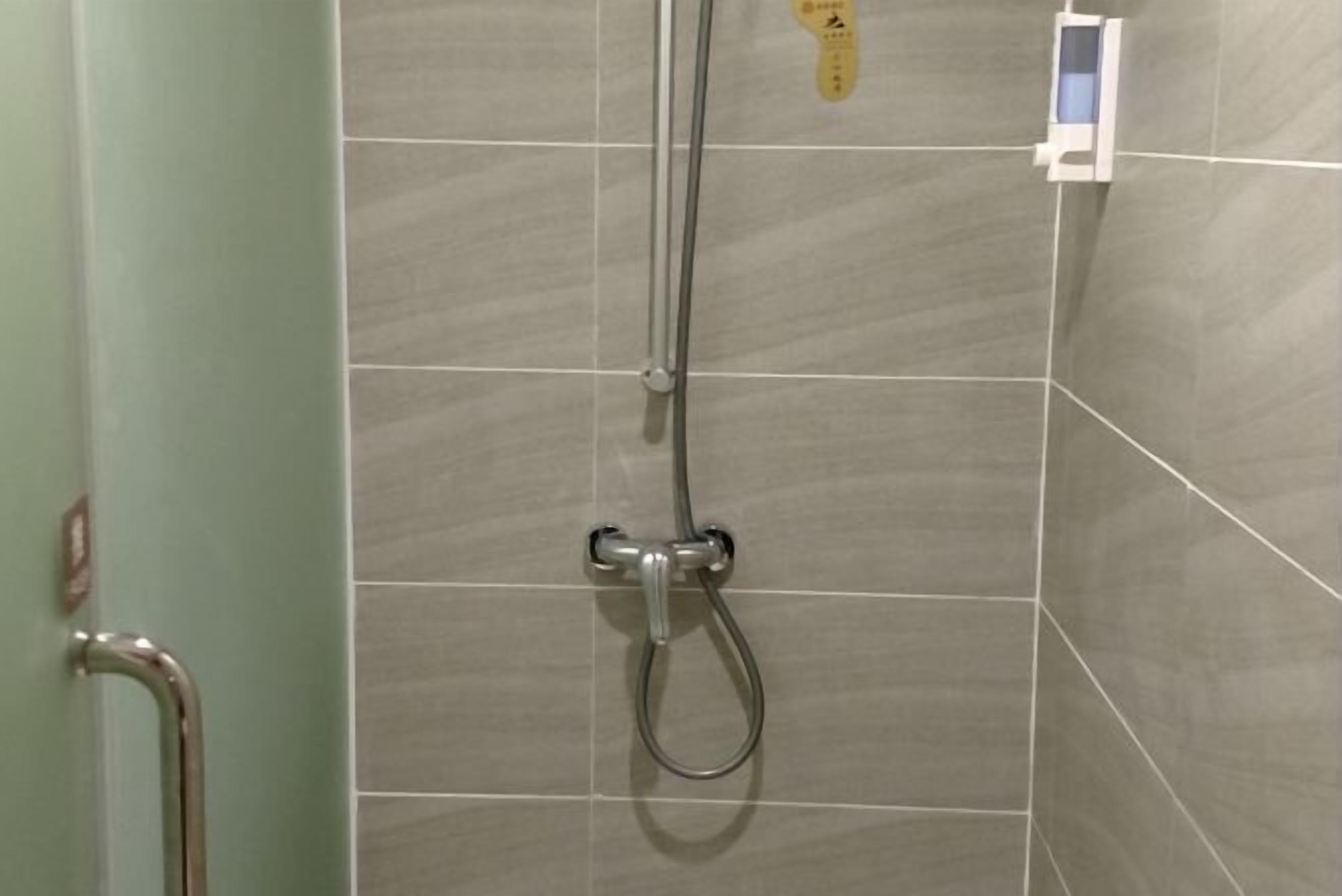 A shower area with a handheld showerhead and a wall-mounted control panel.