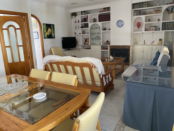 Un salon avec un canapé en bois, une table basse en verre, un téléviseur et une bibliothèque remplie de livres et d’objets décoratifs.