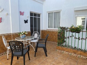 Une terrasse avec une table ronde et des chaises, une fenêtre avec des rideaux et une clôture décorative agrémentée de plantes.