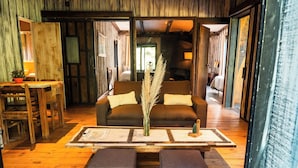 Una habitación acogedora con suelo de madera, un sofá marrón con dos cojines, una mesita con un jarrón de plumas de pampa y un banco de madera.