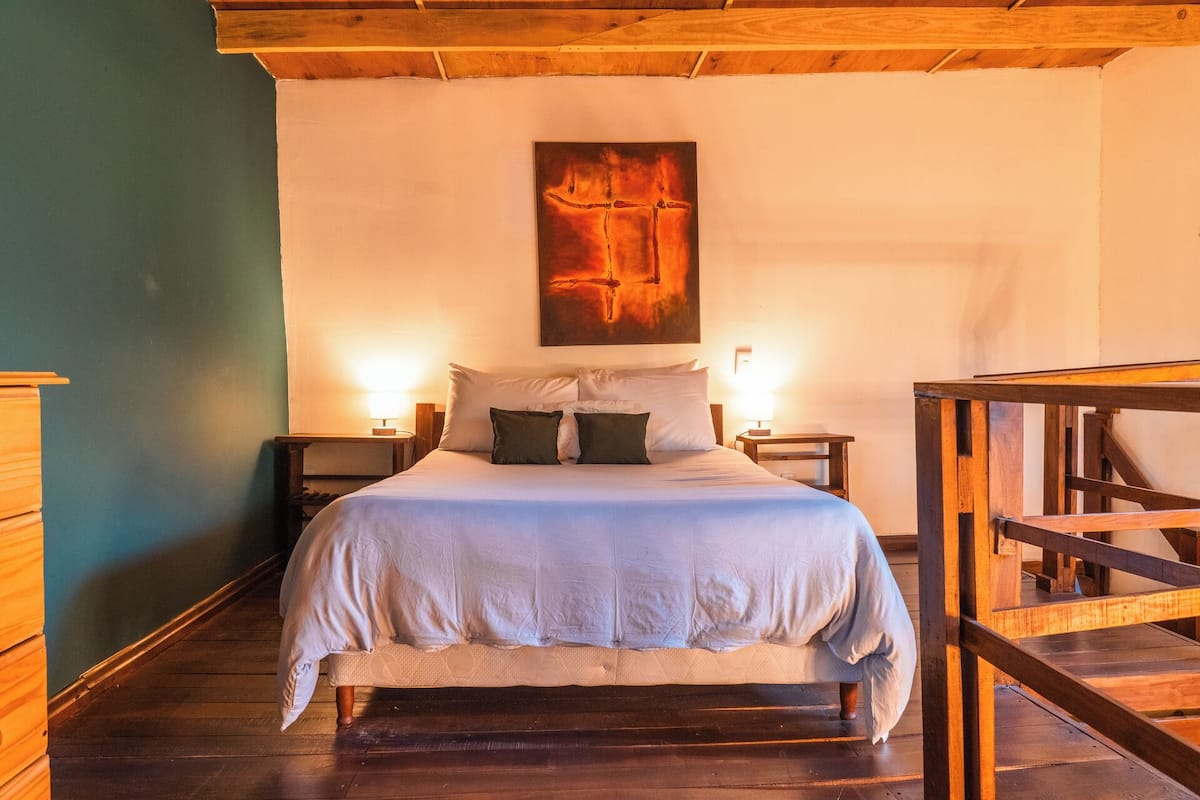 A bedroom with a bed, two bedside tables, a wooden bench, and a painting on the wall.