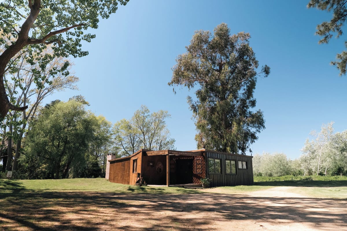 A rustic cabin with a wooden exterior, surrounded by trees and a clear sky.