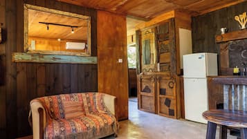 Interior rústico de una cabaña con un sofá, paredes de madera, un espejo, un refrigerador y una mesa de comedor.