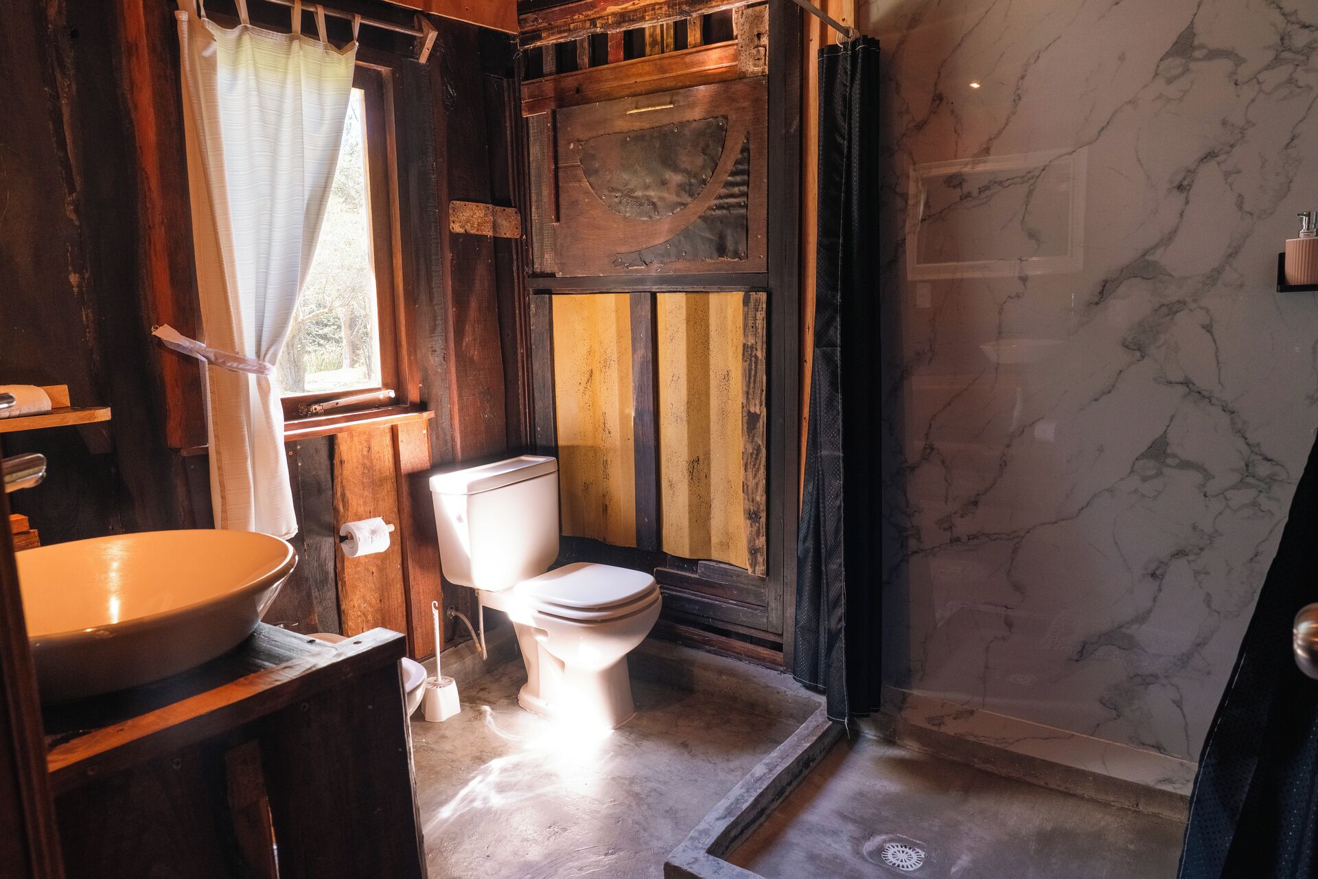 A rustic bathroom with a wooden vanity, a toilet, and a shower area.