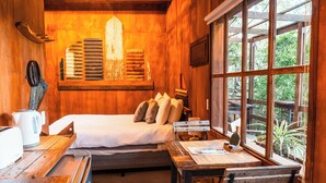 Una habitación de madera acogedora con una cama, una mesa y una ventana con vistas a la vegetación.