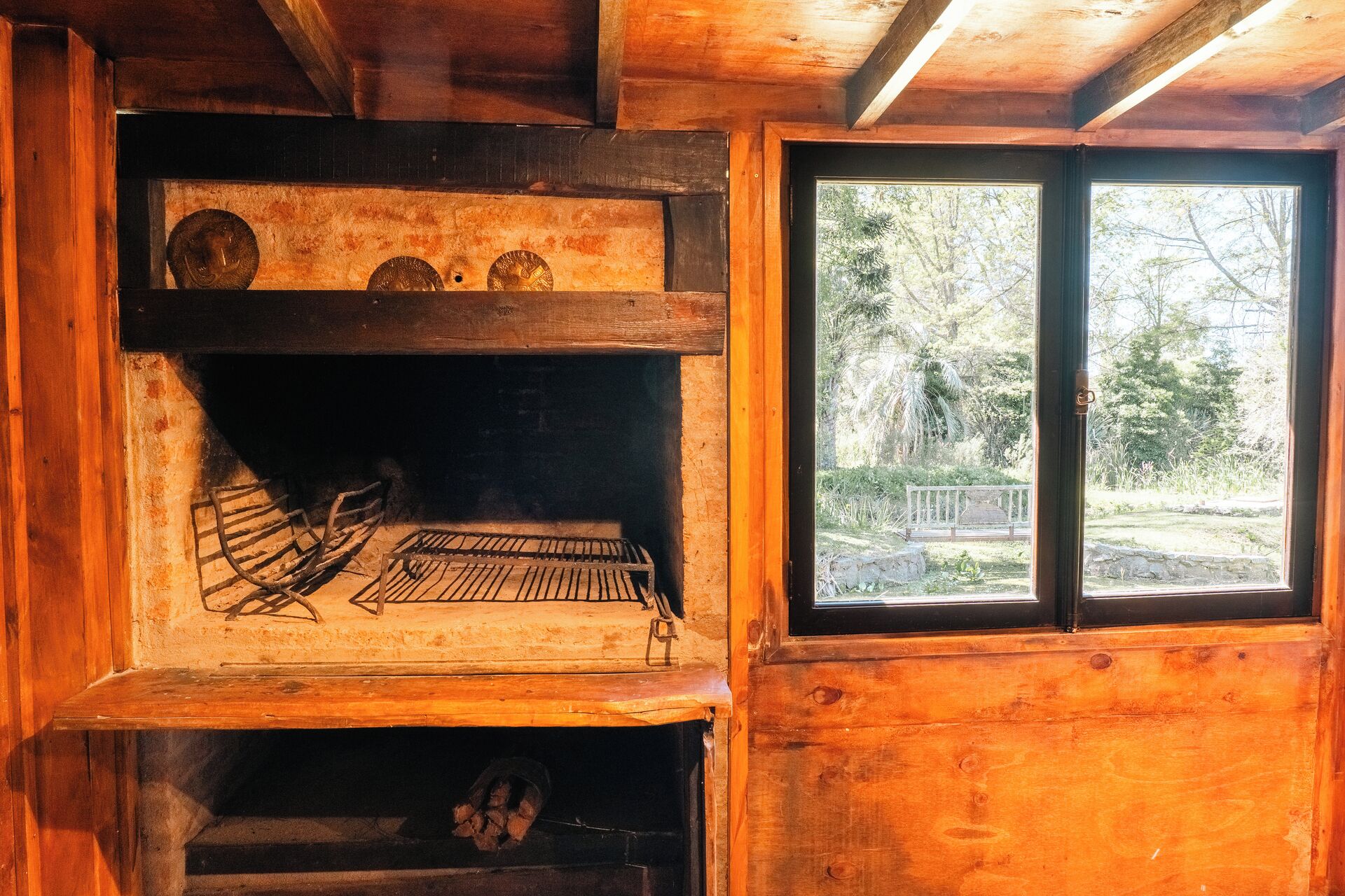 A rustic wooden cabin interior with a fireplace, a window with a view of a forest, and a wooden bench.
