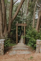 A wooden signpost with the text "Quanta delgardo" at the entrance of a stone pathway surrounded by trees.