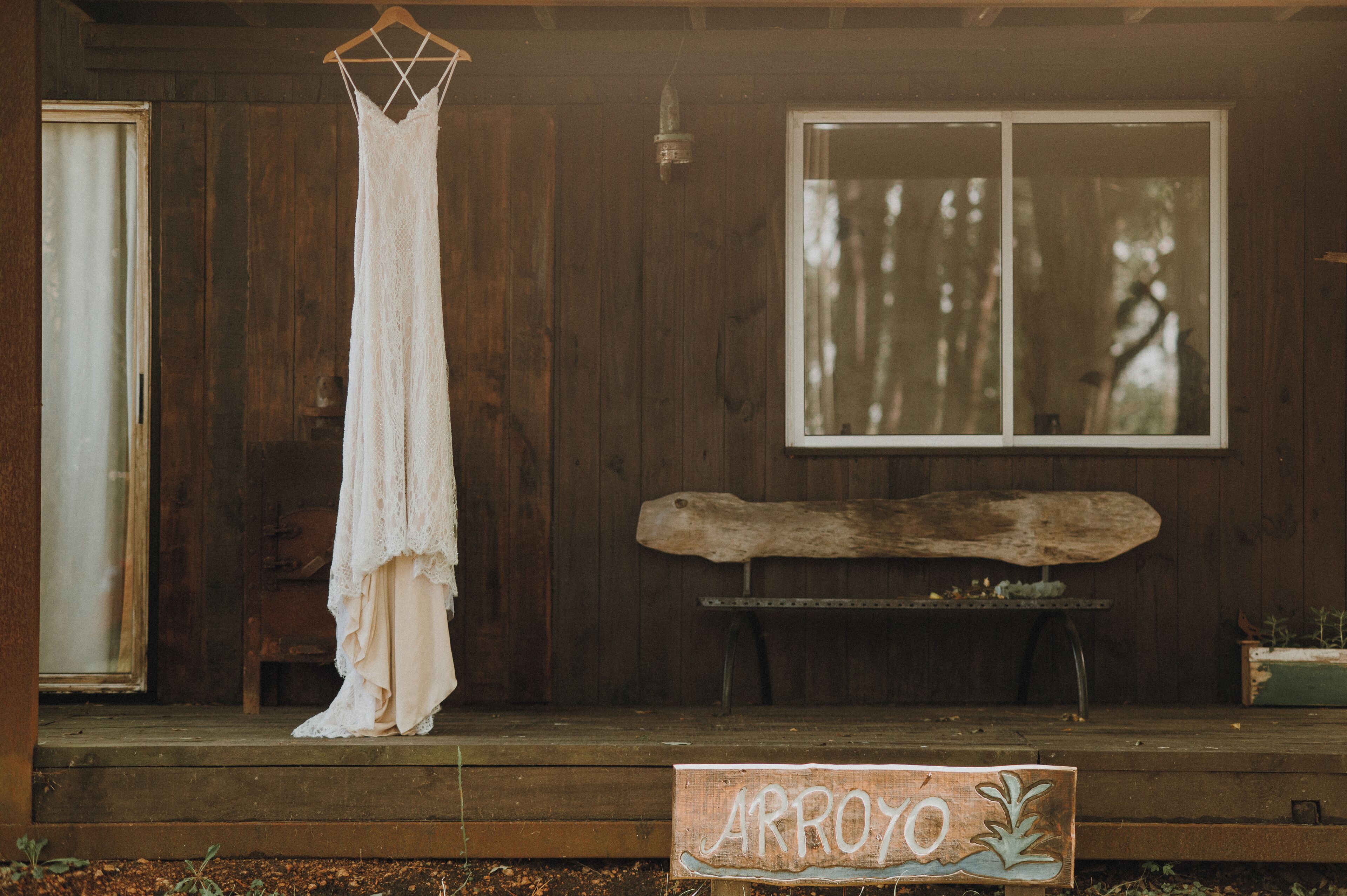 A wooden porch with a hanging white dress, a wooden bench, and a sign that reads "ARROYO".