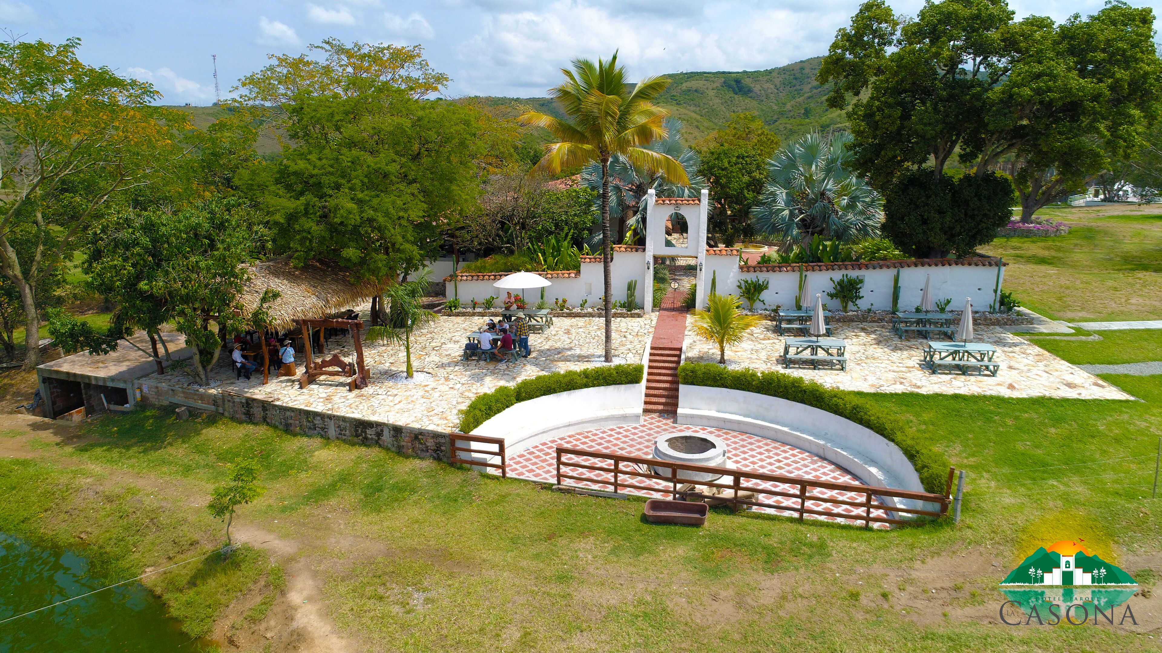A courtyard with a central fountain, stone seating, and a thatched-roof structure.