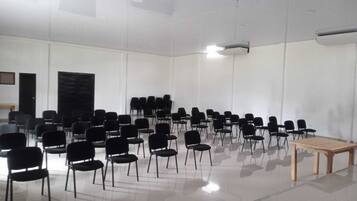 Un amplio salón de conferencias vacío con filas de sillas negras y una mesa de madera.