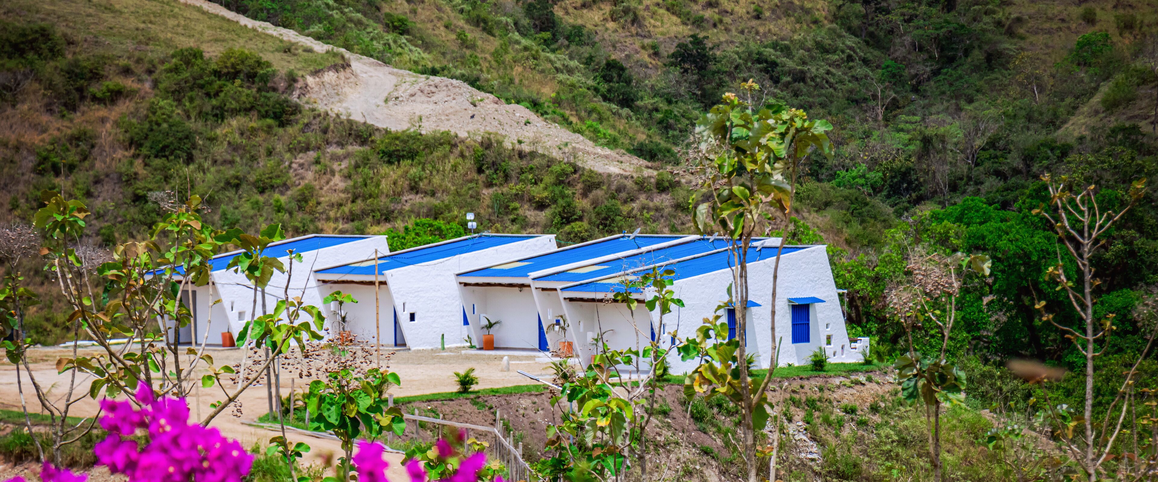 Une rangée de bâtiments blancs aux toits bleus, entourés de verdure et de collines.