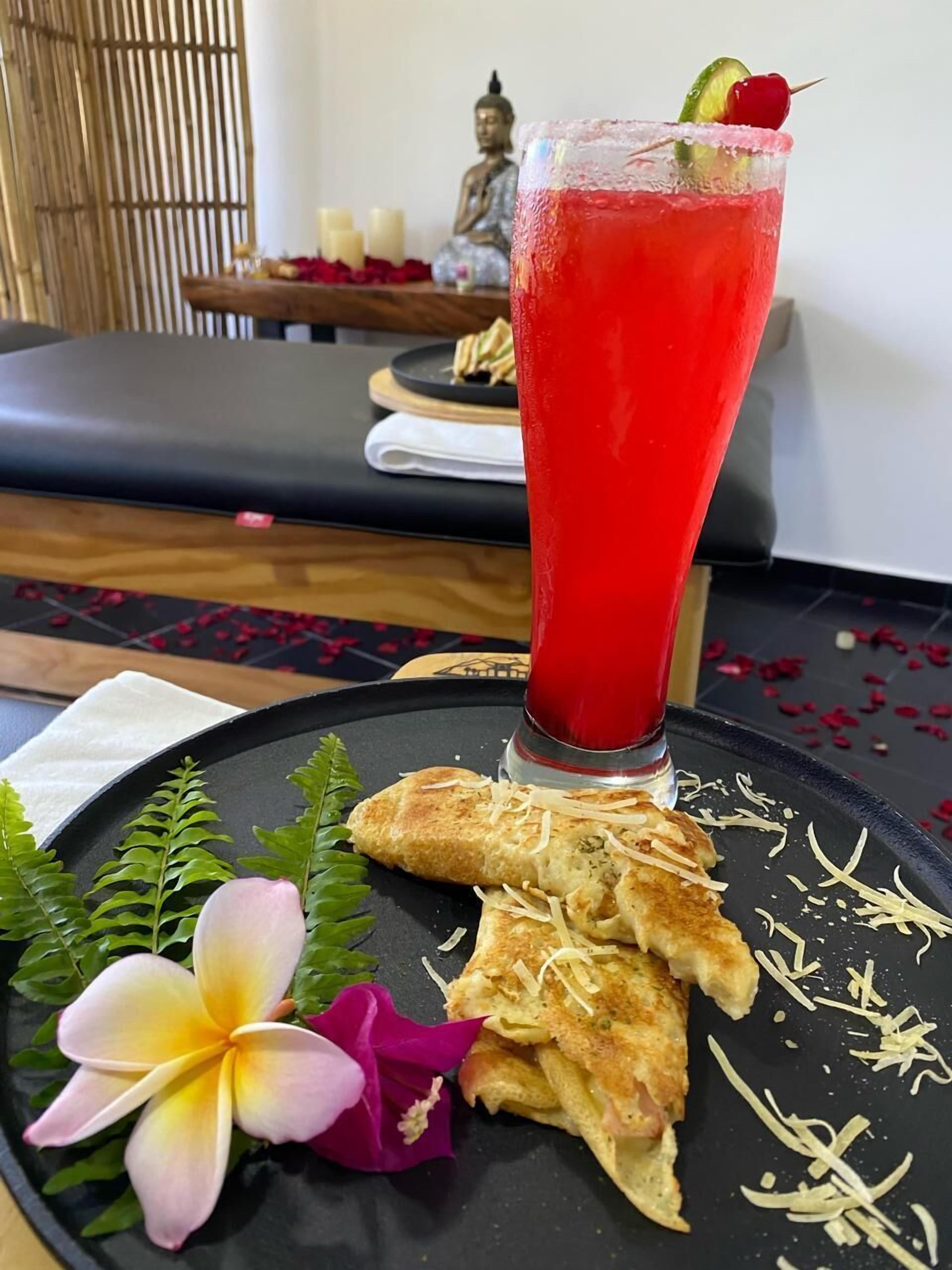 A table with a red drink, a plate with food, and a Buddha statue in the background.