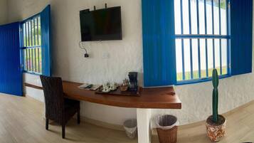 Una habitación con un escritorio de madera, una silla, un televisor y una ventana con contraventanas azules.