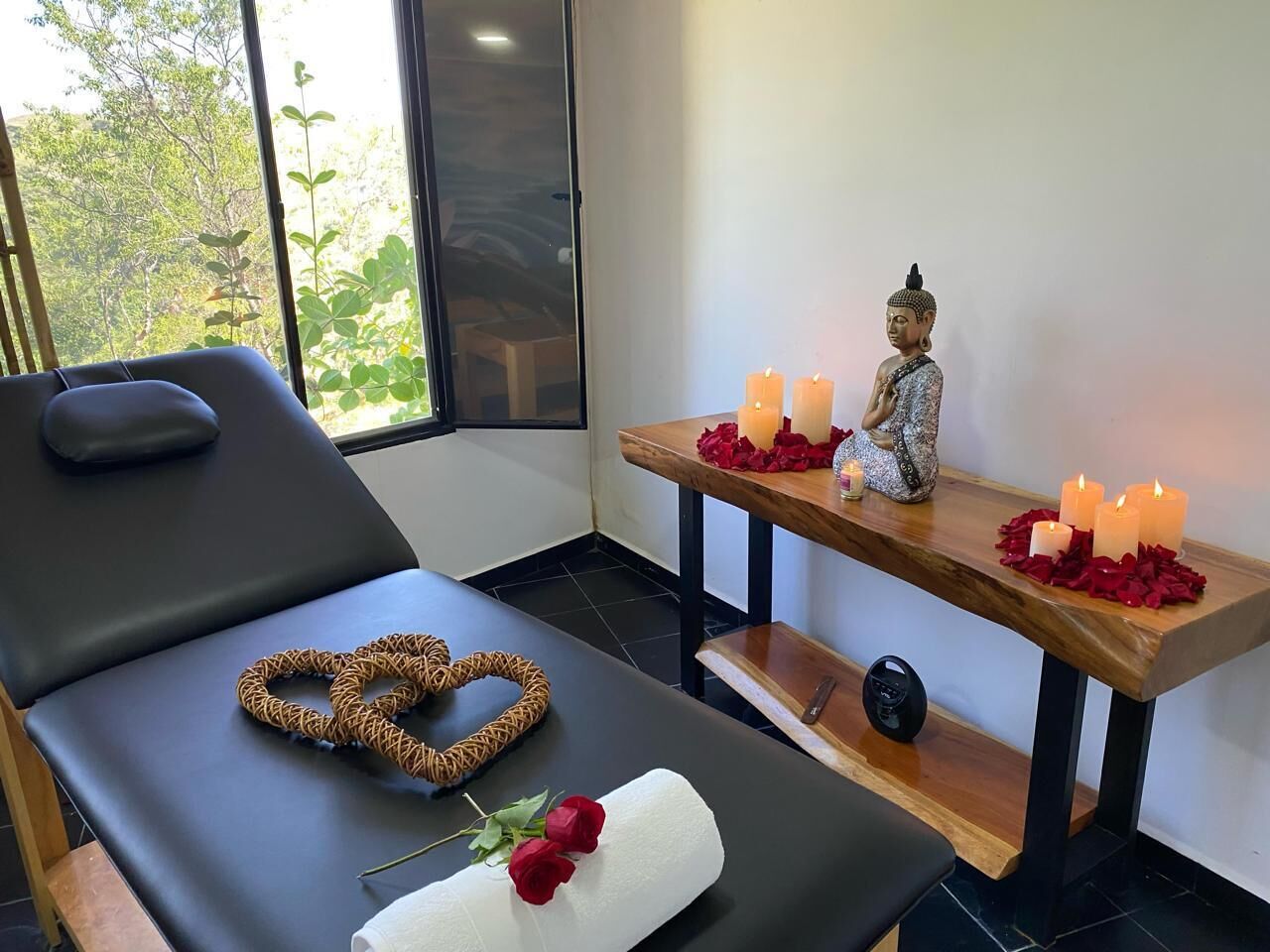 A massage therapy room with a massage table, a decorative heart-shaped object, a rose, and a statue on a wooden shelf with candles.