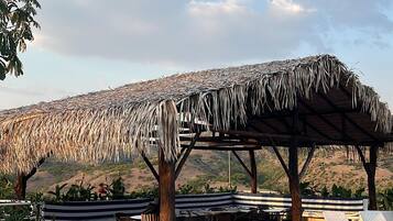 A pool area with a thatched roof structure, lounge chairs, and a tiled deck.