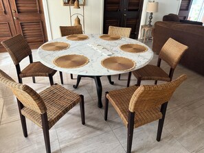 A round table with a marble top surrounded by eight wicker chairs with dark legs.