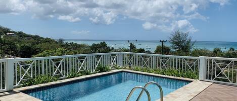 Piscina retangular com grade branca, rodeada por um deck ladrilhado.