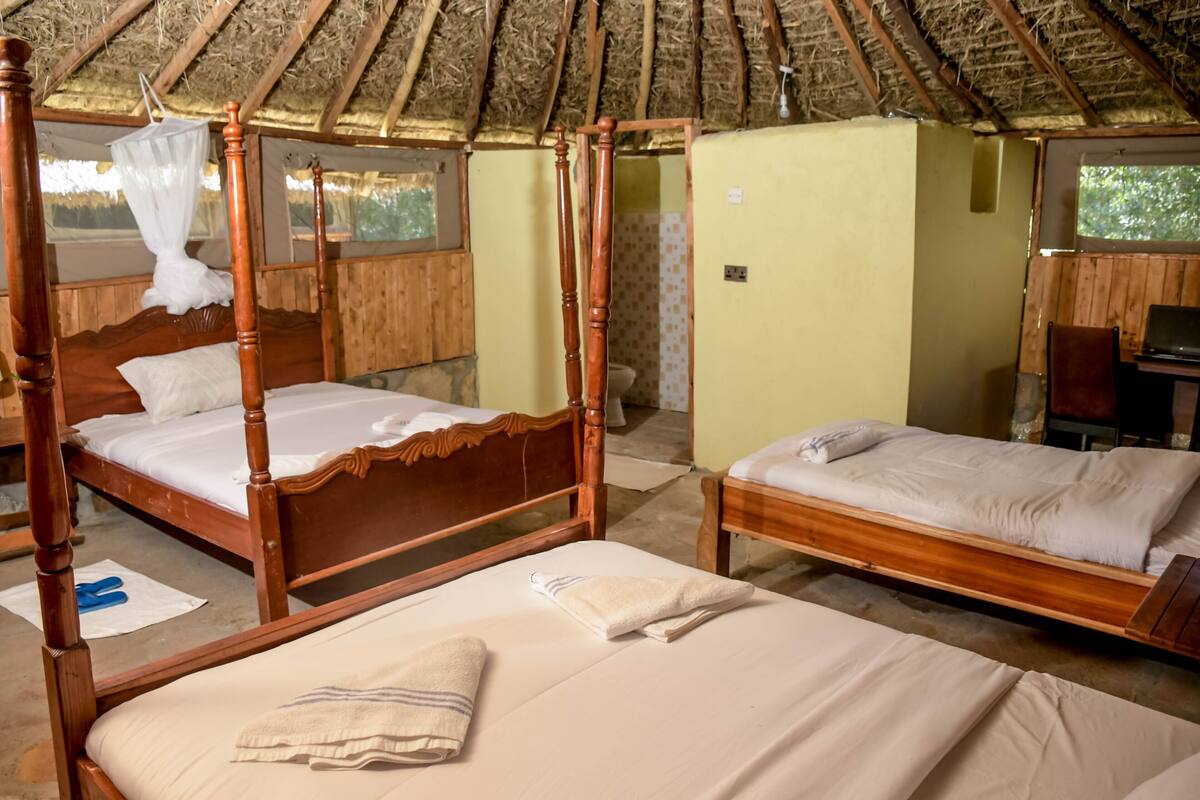 A room with two wooden beds, a thatched roof, and a small desk with a laptop.