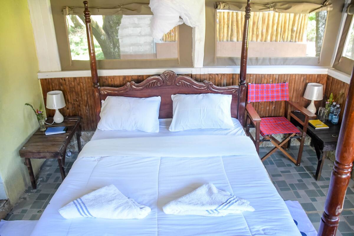 A four-poster bed with white linens, a wooden headboard, and a red checkered chair.