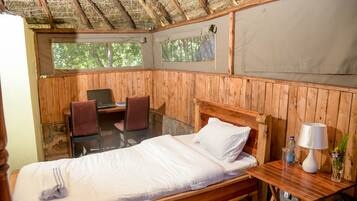 A wooden room with a bed, a desk, and a chair. There are windows and a view of trees outside.