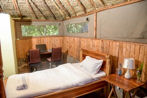 Una habitación de madera con una cama, un escritorio y una silla. Hay ventanas y se ve un paisaje de árboles fuera.