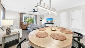 A modern living room with a round wooden table, a sofa, and a dining area with a chandelier. - 🐟Bikes Included-Cassine Gardens 273-30A (Santa Rosa Beach)