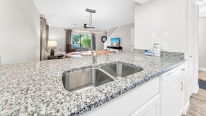 A modern kitchen with granite countertops, stainless steel sink, and white cabinetry. - 🐟Bikes Included-Cassine Gardens 273-30A (Santa Rosa Beach)