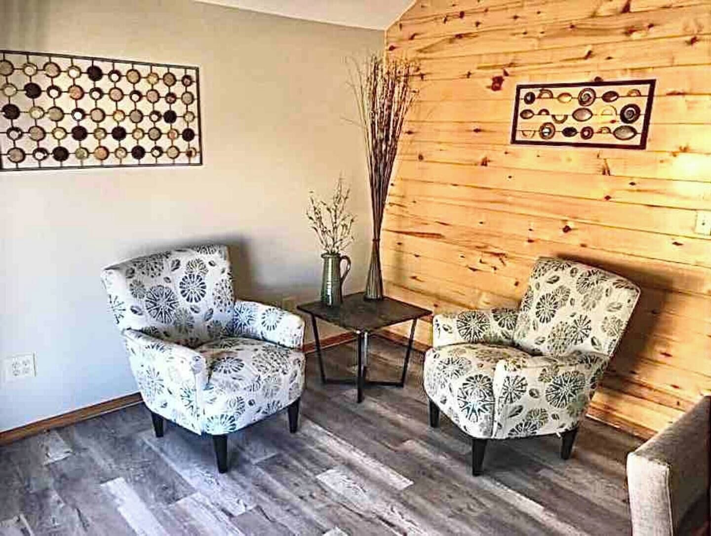 A room with two patterned armchairs, a small table with a vase, and wooden walls with circular designs.