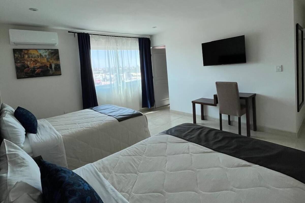 Ein Hotelzimmer mit zwei Betten, einem Schreibtisch, einem Stuhl, einem Fernseher und einem Fenster mit Vorhängen.