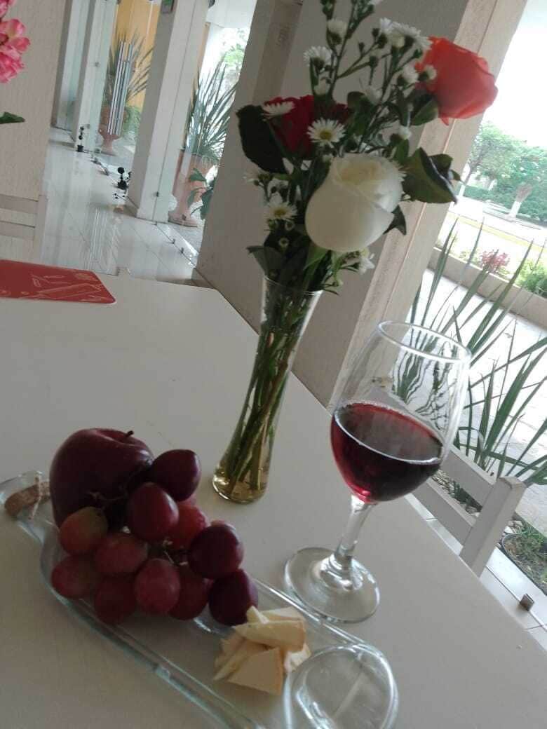 A table with a glass of red wine, a plate of grapes, and a vase of flowers.