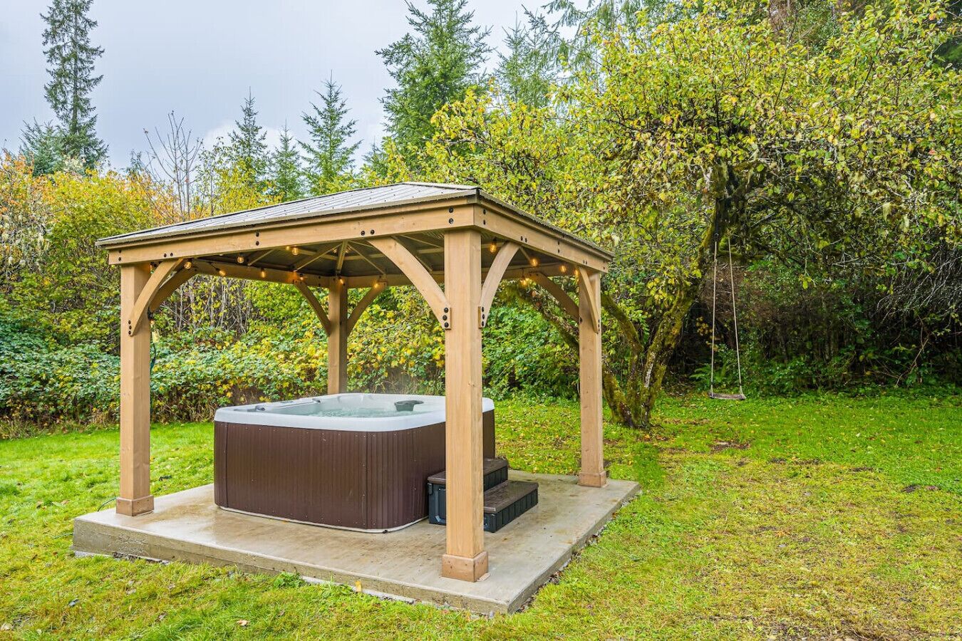 Un jacuzzi bajo un porche de madera en un jardín.