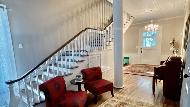 A spacious living area with a staircase, red armchairs, a patterned rug, and a chandelier. - Historic suite 3 (Magnolia)