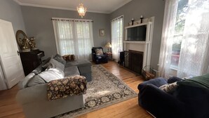 A living room with a grey sectional sofa, a blue armchair, a fireplace, and a chandelier. - Historic suite 3 (Magnolia)