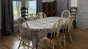 A dining room with a chandelier, wooden chairs, a table with a floral tablecloth, and a view of the outdoors through large windows. - Historic suite 3 (Magnolia)