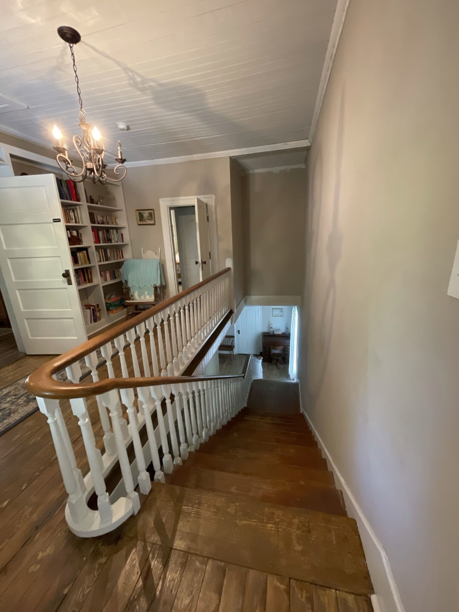 A wooden staircase with white railings leading to a landing with a chandelier and a bookshelf.