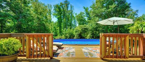 A wooden deck with a pool, surrounded by trees and a view of a blue sky.
