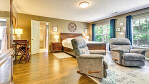 A bedroom with a wooden floor, a bed with a headboard, two armchairs, a nightstand, a dresser, and a window with curtains. - Browns Summit Vacation Rental w/ Fire Pit! (Browns Summit)