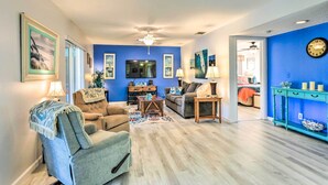 A living room with a blue accent wall, a ceiling fan, a flat-screen TV, and a dining area with a teal console table. - Venice Home w/ Private Pool, 7 Mi to Beach! (Venice)
