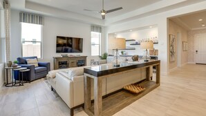 Amplia sala de estar con una isla central, un sofá, un televisor y una zona de cocina con barra.