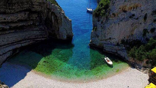 Un paysage côtier caractérisé par des falaises rocheuses, des eaux turquoise et limpides, et un bateau ancré près du rivage.