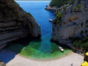 A coastal landscape with rocky cliffs, clear turquoise waters, and a boat anchored near the shore. - Apartments Katarina - Two Bedroom Apartment with Terrace (Vis)