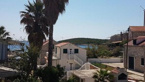 Un quartier résidentiel situé sur la côte, caractérisé par des bâtiments en pierre, un palmier imposant et une vue dégagée sur la mer.