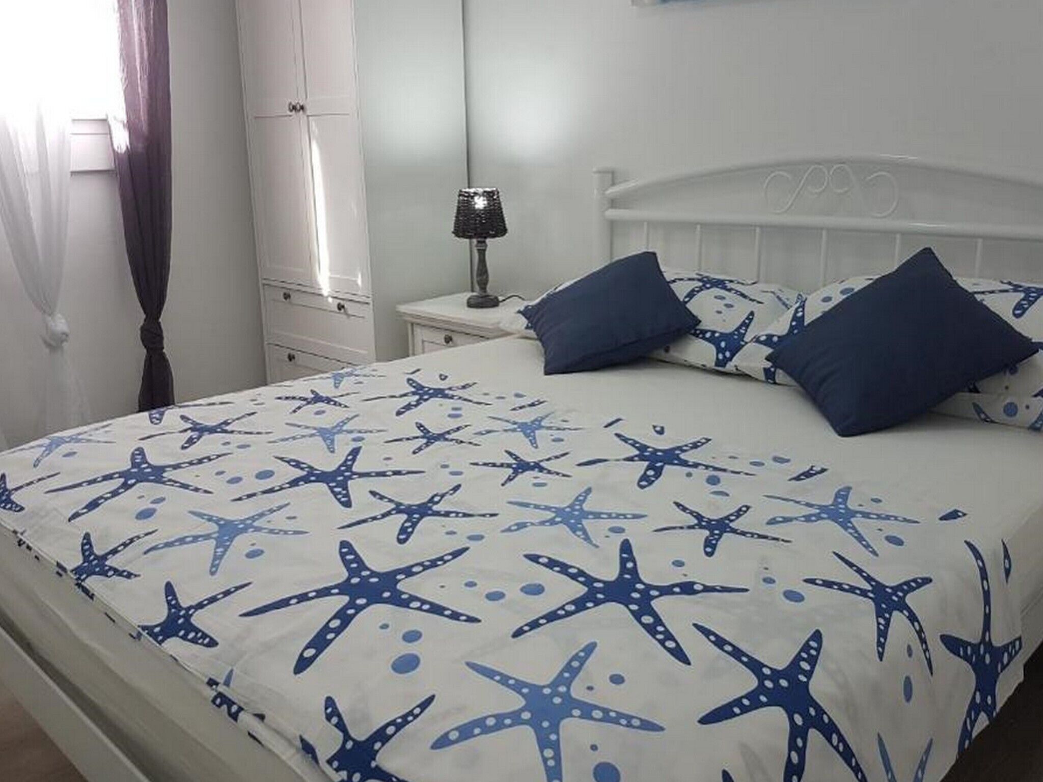 A bedroom with a bed featuring a starfish pattern, a white headboard, and two bedside tables with lamps.