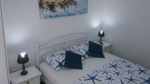 Ein Schlafzimmer mit einem Bett, zwei Nachttischen, einer Lampe auf jedem und einem Gemälde eines Leuchtturms an der Wand.