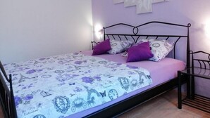 A single bed with a metal frame, a floral-patterned bedspread, and two purple pillows.