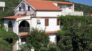 A white building with a red-tiled roof, a balcony, and a small attached structure.
