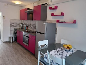 A compact kitchen with a washing machine, a stove, a refrigerator, and a dining table with chairs.